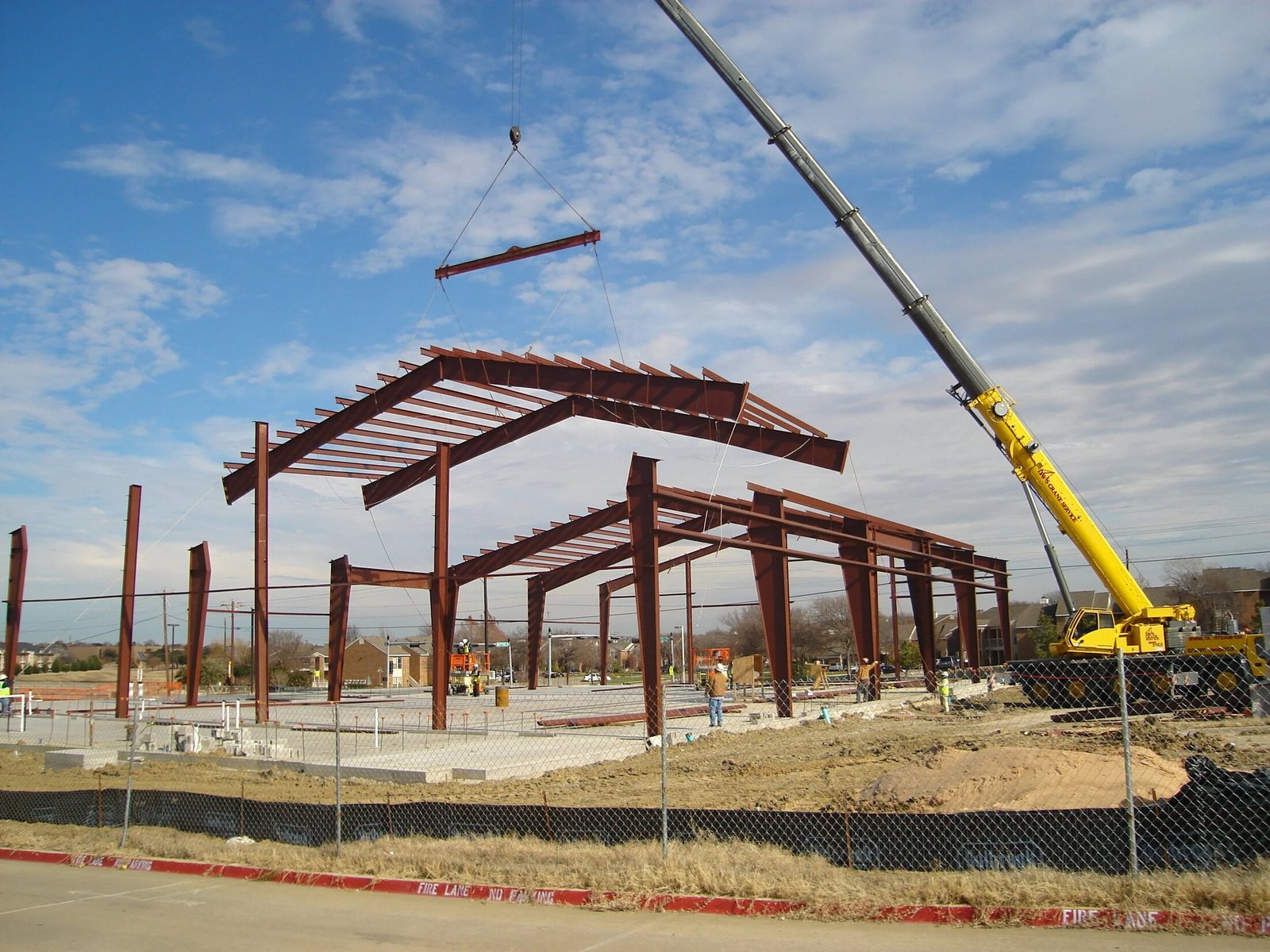 Red structural steel frame and yellow crane at a facility expansion